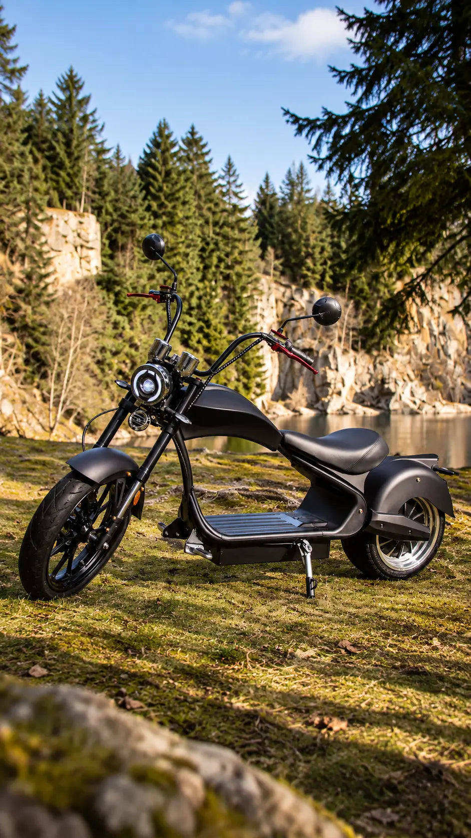 E-Chopper 6.0 Premium in Schwarz mit breiten Reifen und LED-Rundscheinwerfer, abgestellt auf einer Wiese am See